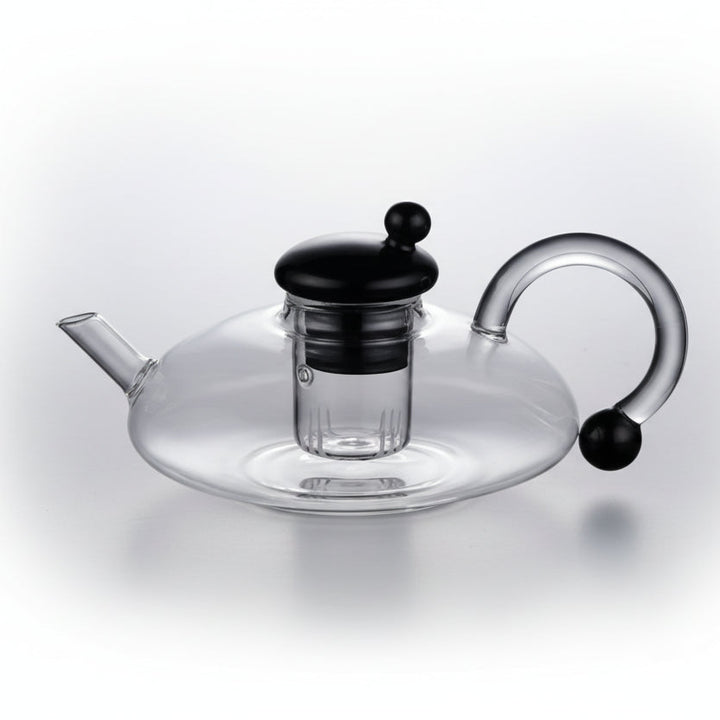 Clear glass teapot with black lid and handle on a white background